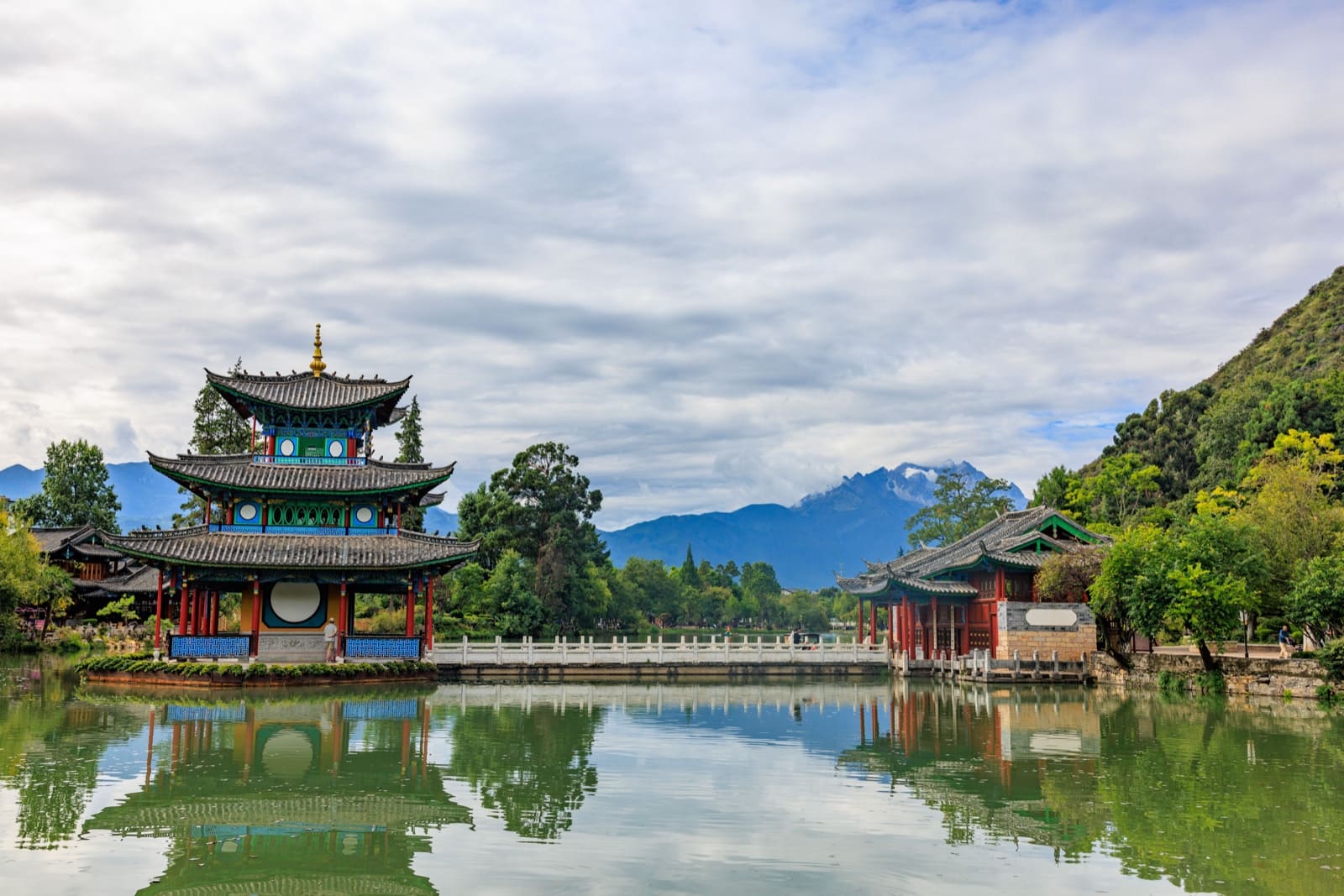 Traditional Chinese stone bridge reflected in a lake at the Black Dragon Pool in Lijiang, Yunnan, with Jade Dragon Snow Mountain in the background sky